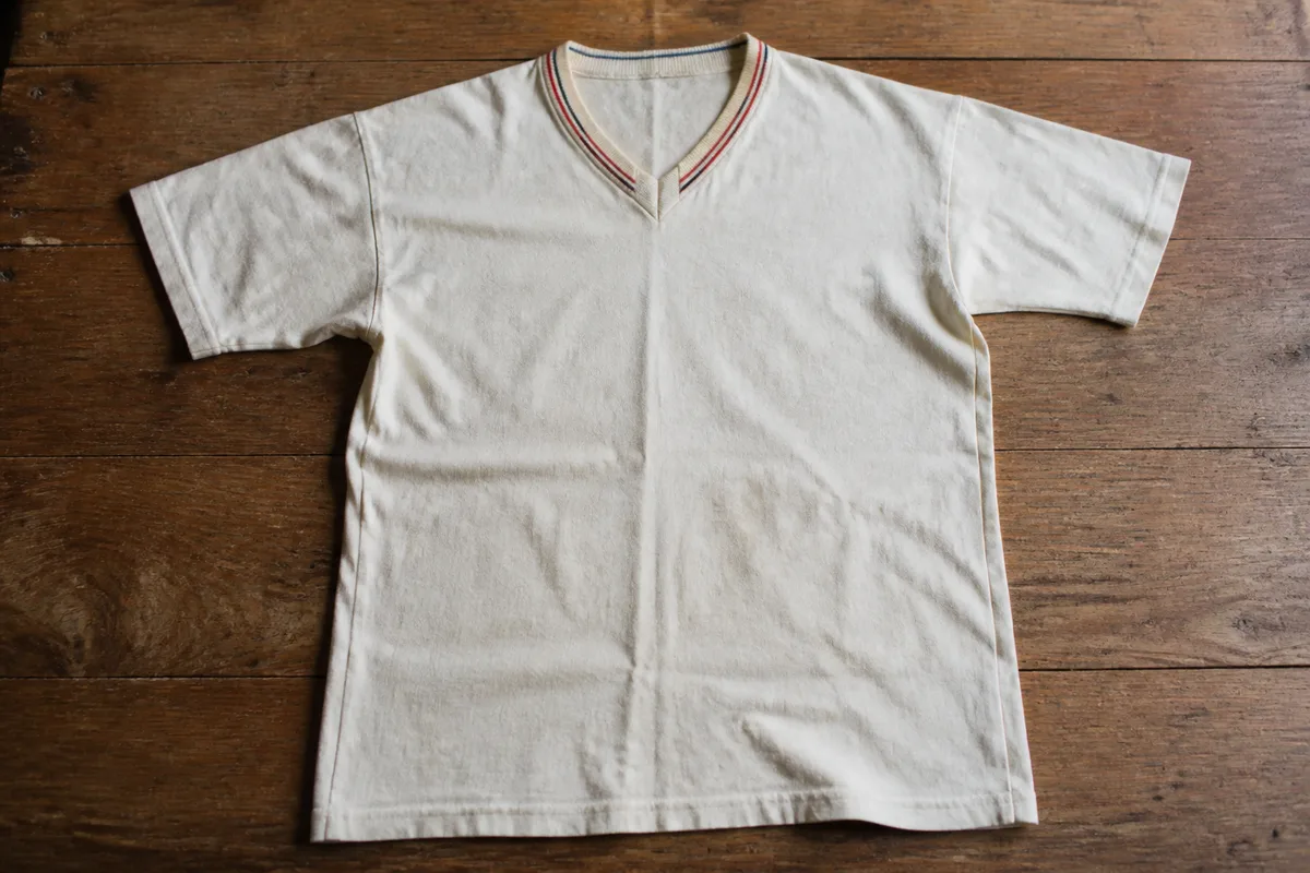 Chemise de football blanche ancienne posée à plat sur une table en bois avec un liseré coloré au col